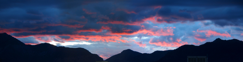 [Just above the mountain line is a series of pink tinted undersides to dark blue clouds. This is several photos stitched together.]